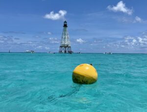 A yellow mooring buoy in the foreground and a white and black lighthouse in the background.